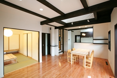 ＬＤＫ。太い濃い茶の梁が白い壁を引き締めるアンティーク調の雰囲気。家族がいつも一緒に過ごす、やすらぎの空間。暗くならないように、床にはピンク色が美しいサクラ材を使用。