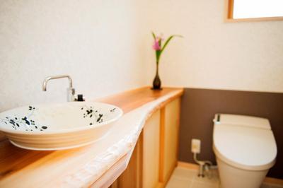 1枚板のカウンターに陶器の手洗いボウルを据えた広いトイレ。床はお手入れが楽なタイルです。