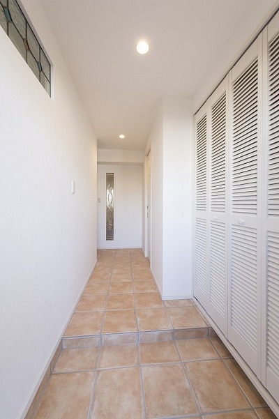 玄関収納は通気がよいルーバー扉に。玄関のテラコッタタイルを廊下まで続けさせ、広く見せています。