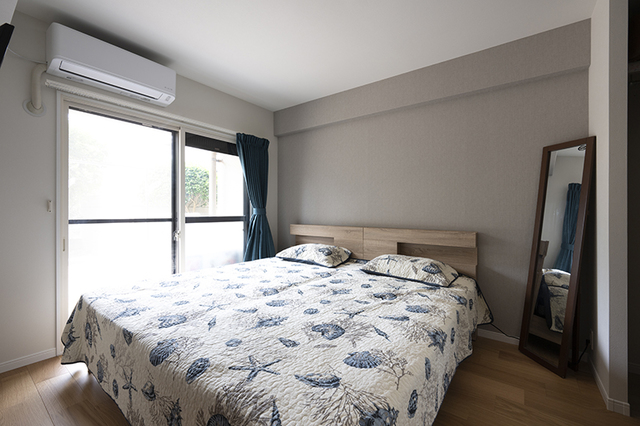 グレーのアクセントクロス、ブルーのベットカバーとカーテン、シンプルで落ち着いた寝室。
そして限られたスペースに壁掛けのテレビを設置。