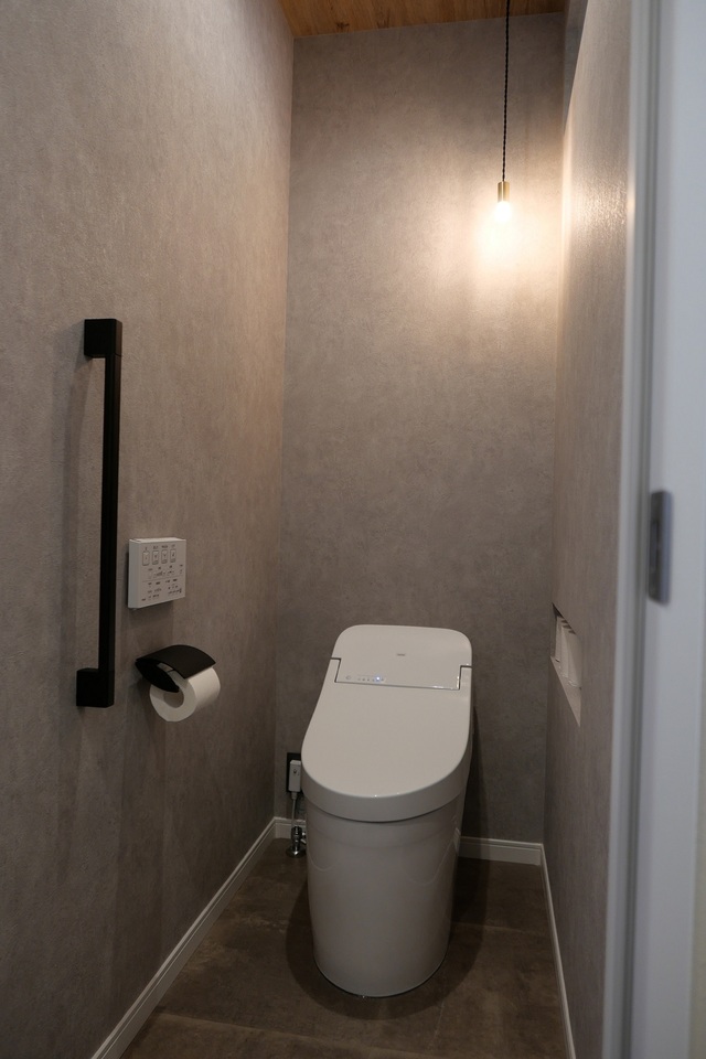 グレーの床と壁に合わせ、天井には木目をチョイス。優しい光のペンダントライト。外壁に面していないため、上部にFIXガラスを入れ脱衣所から自然光を取り入れるように工夫しています。
収納棚を設けずスッキリみせるため、トイレットペーパーを収納できるサイズのニッチを造りました。